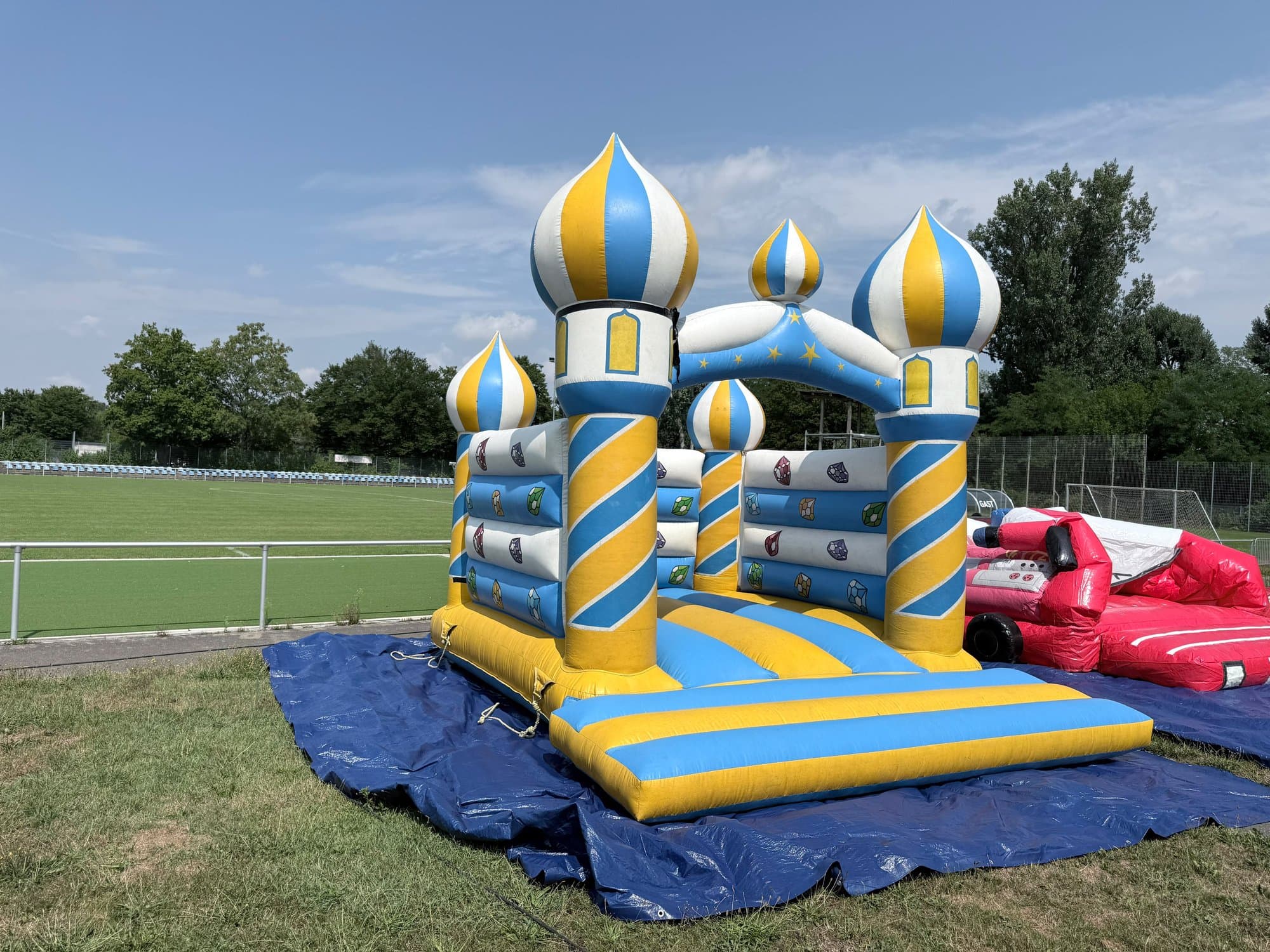Hüpfburg Orient-Schloss mit gelb-blauen Zwiebeltürmen auf einer Plane neben einem Sportplatz