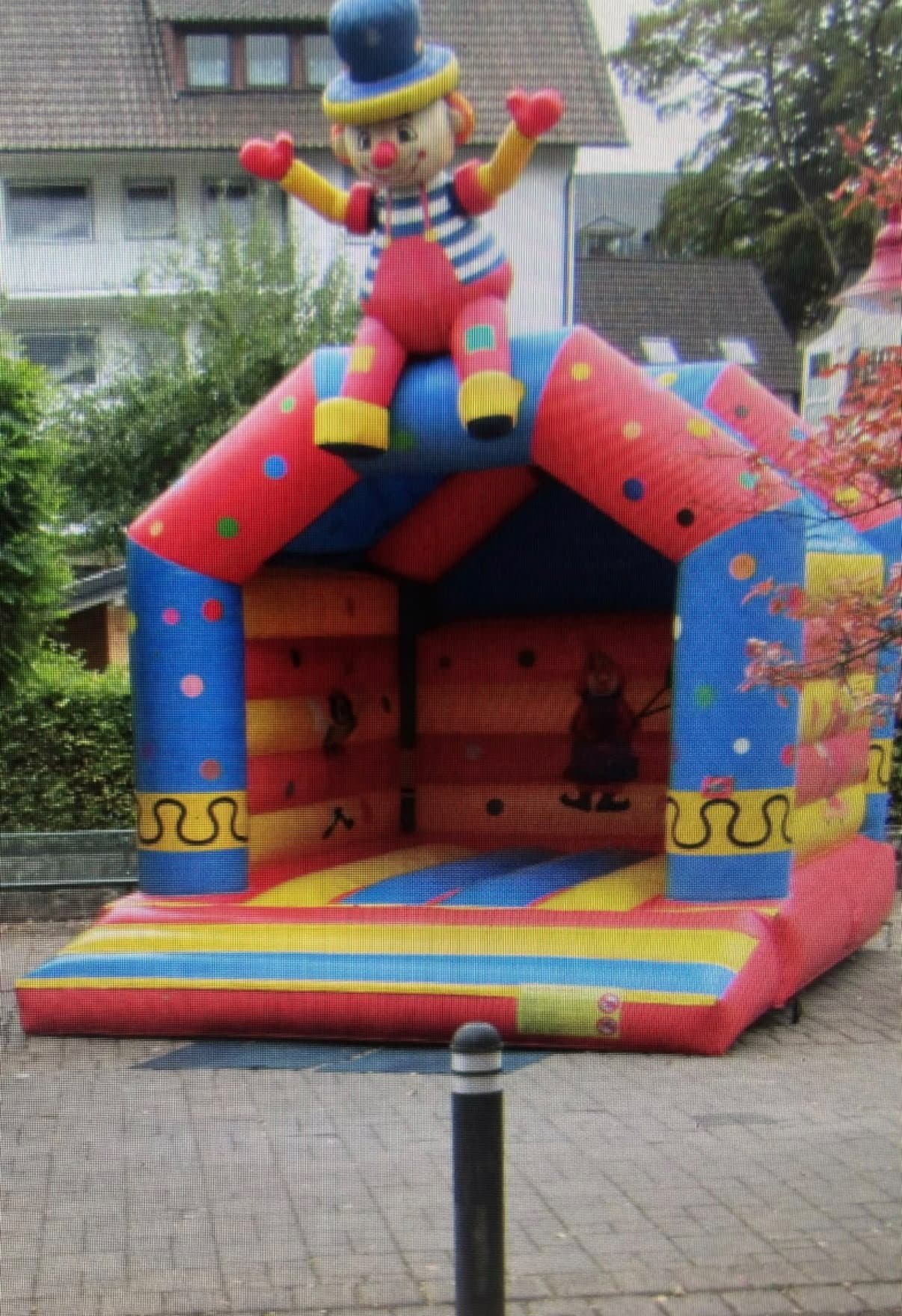Hüpfburg mit großer Clown-Figur auf dem Dach, aufgebaut auf Pflaster