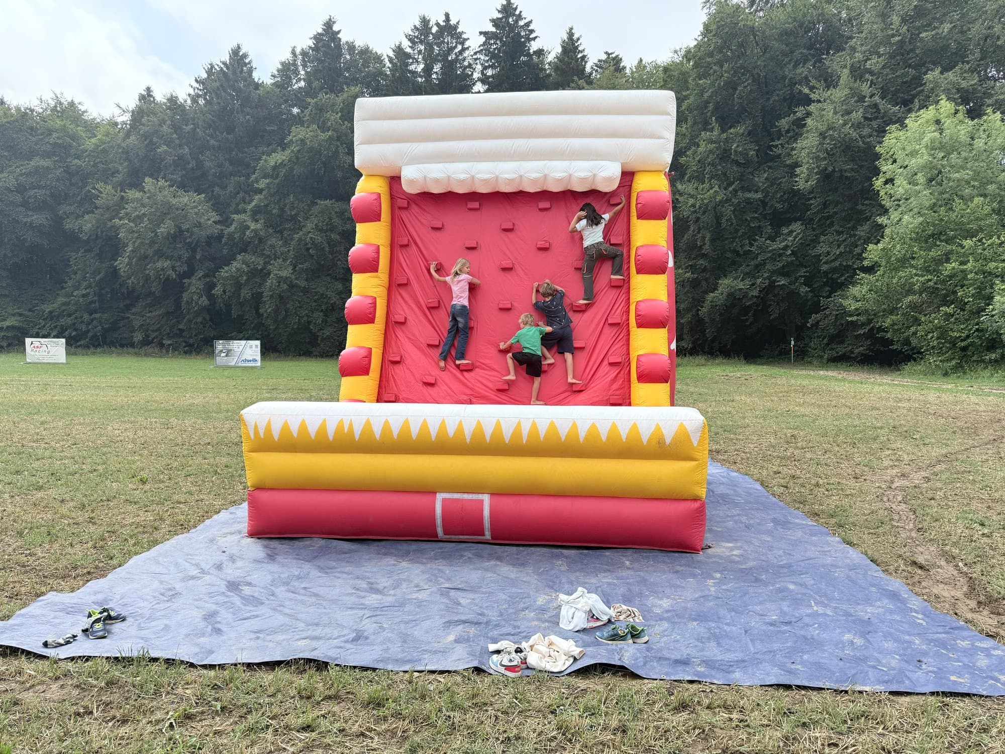 Aufblasbare Kletterwand auf einer großen Wiese, Kinder klettern, nur von hinten zu sehen